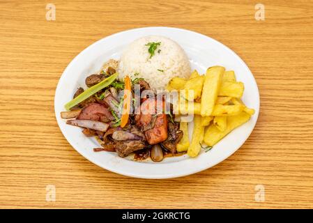 Stilvolle Präsentation eines traditionellen peruanischen Rezepts für gebratenen Filet mit Gemüse, einer Garnierung aus hausgemachten Kartoffeln und einer Schüssel umgedrehtem Stockfoto