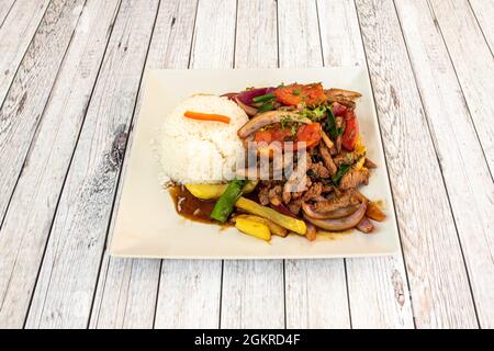 Peruanisches Rezept für Lomo Saltado mit Pommes Frites, weißem Reis, roten und grünen Paprika Twists, Zwiebeln und Petersilie auf einem weißen Teller Stockfoto