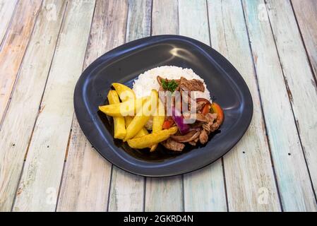 Hausgemachter Lomo Saltado mit hausgemachten pommes frites und Rührgemüse und Schweinefilet auf schwarzem Teller Stockfoto