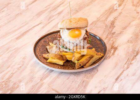 Toller Kalbsburger mit Spiegelei und köstlichem Eigelb, gebratenem geräuchertem Speck und Pommes auf dem Marmortisch Stockfoto