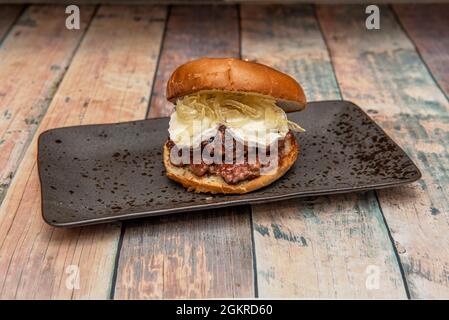 Burger mit doppeltem Rindfleisch, doppeltem Ziegenkäse und karamellisierter Zwiebel auf einem schwarzen Tablett Stockfoto