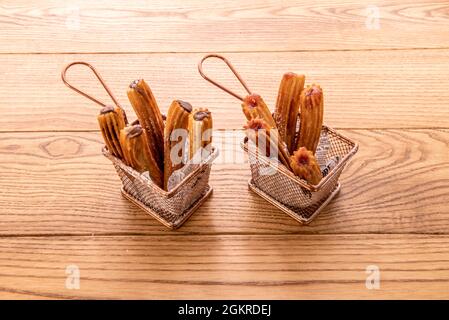 Metallkörbe voller Churros, gefüllt mit Schokolade und Himbeermarmelade auf einem Holztisch Stockfoto