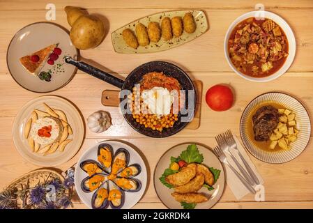 Bild von oben mit beliebten spanischen Gerichten. Kichererbsen-Eintopf mit Ei und Ratatouille, Madrider Kutteln, Backenbraten mit Bratkartoffeln, galizisch gedünstet Stockfoto