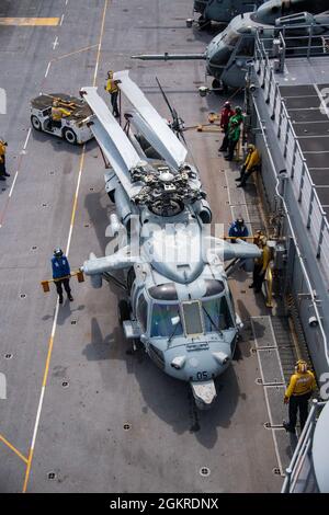 PHILIPPINISCHE SEEFAHRER (20. Juni 2021), die dem nach vorne eingesetzten amphibischen Sturmschiff USS America (LHA 6) zugewiesen wurden, sehen auf dem Flugdeck des Schiffes einen Hubschrauber der MH-60S Sea Hawk vom Helicopter Sea Combat Squadron (HSC) 25. Amerika, das führende Schiff der America Amphibious Ready Group, arbeitet zusammen mit der 31. Marine Expeditionary Unit im Einsatzgebiet der 7. US-Flotte, um die Interoperabilität mit Verbündeten und Partnern zu verbessern und als einsatzbereite Einsatztruppe zur Verteidigung von Frieden und Stabilität in der Indo-Pazifik-Region zu dienen. Stockfoto