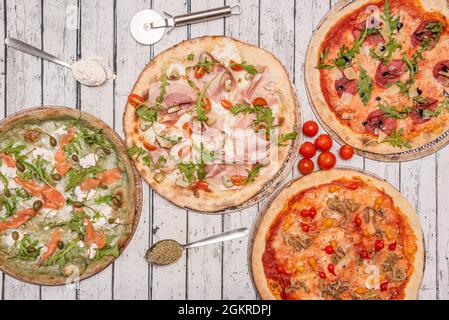 Bild von oben von italienischen Pizzas verschiedener Geschmacksrichtungen mit Mehl und Orangen in Löffeln. Rucola und Käse mit norwegischem Lachs, Schinken und Lende und che Stockfoto