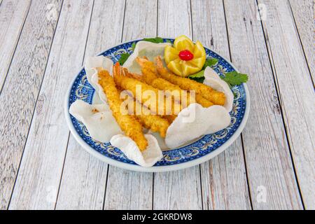 Gebratene Tempura-Garnelen in einem chinesischen Restaurant mit Garnelenbrot auf einem blaukantigen Teller und einer in Scheiben geschnittenen Zitrone. Stockfoto