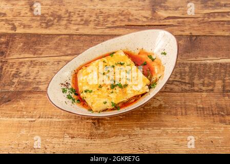 Schöne Schüssel mit italienischer Lasagne gefüllt mit Rindfleisch mit viel Petersilie und viel Pomodoro-Sauce auf Holztisch Stockfoto