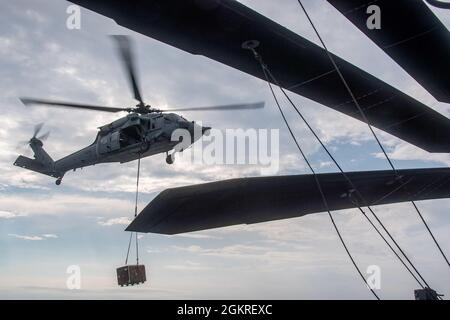 PHILIPPINISCHES MEER (21. Juni 2021) ein Hubschrauber der MH-60S Sea Hawk vom Helicopter Sea Combat Squadron (HSC) 25 liefert während einer Auffüllung auf See Ladung zum Flugdeck des nach vorne eingesetzten amphibischen Sturmschiffes USS America (LHA 6). Amerika, das führende Schiff der America Amphibious Ready Group, arbeitet zusammen mit der 31. Marine Expeditionary Unit im Einsatzgebiet der 7. US-Flotte, um die Interoperabilität mit Verbündeten und Partnern zu verbessern und als einsatzbereite Einsatztruppe zur Verteidigung von Frieden und Stabilität in der Indo-Pazifik-Region zu dienen. Stockfoto