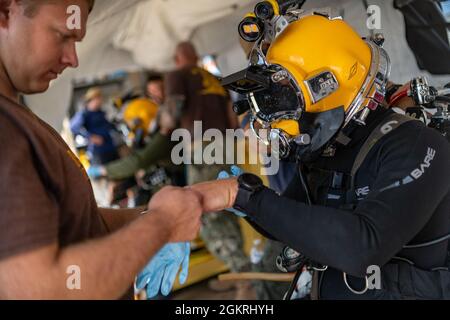 VIRGINIA BEACH, VA. – (21. Juni 2021) Navy Diving 2nd Class Matthew McDorman pflegt den Navy Diving 1st Class Mark Powell, bevor er Tauchoperationen an der Oberfläche durchführt. Beide sind der Mobile Diving Salvage Unit (MDSU) 2, Firma 2-5, zugeordnet. MDSU 2, gegründet von der Joint Expeditionary Base Little Creek - Fort Story, ist eine kampfbereite Expeditionstruppe, die weltweit zur Unterstützung aller Tauch- und Bergungsoperationen eingesetzt werden kann. Stockfoto