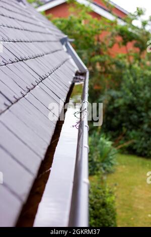Ein Porträt einer verstopften Dachrinne voller Regenwasser an einem regnerischen und bewölkten Tag. Der Boden des Abflusses ist voller Blätter und anderer natürlicher Waste Stockfoto