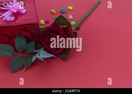 Nahaufnahme rote Rose auf einem Tisch in der Nähe Geschenk-Box mit Band Schleife in rotem Hintergrund platziert. High-Angle-Ansicht. Design für valentinstag, Jubiläum oder Stockfoto