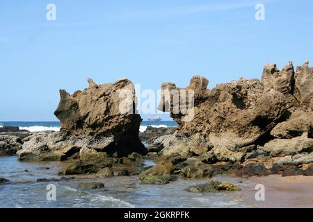 Felsen am Strand mit einem Boot vor der Küste im Hintergrund auf dem indischen Ozean, Umdloti, Durban, Nordküste, Südafrika Stockfoto