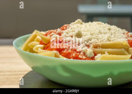 Beliebtes Rezept für Kinder von Makkaroni mit Tomaten und geriebenem Käse auf einem blauen Teller Stockfoto