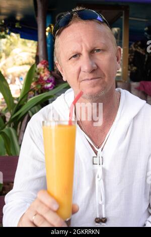 Reifer europäischer Mann, der im Café mit Mango-Cocktail sitzt Stockfoto