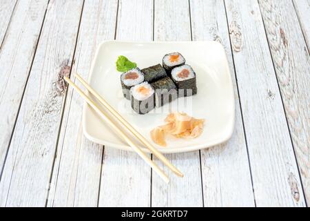 Serviert norwegisches Lachs-Maki-Sushi, roten Thunfisch und japanischen Essig-Reis, gerollt mit Nori-Algen, Wasabi, Ginseng und chinesischen Essstäbchen Stockfoto