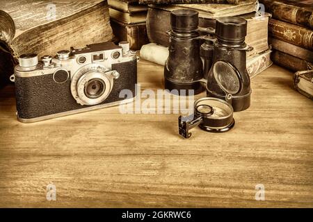 Sepiafarbisches Bild eines Holztisches mit alten Büchern, Kamera, Fernglas und Kompass Stockfoto