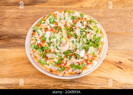 Pizza mit viel Rucola und viel Parmesan in dünnen Krustenflocken und Mozzarella mit gehackter Tomate Stockfoto