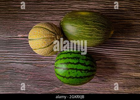 Zwei Melonen und eine Wassermelone von oben betrachtet. Kleine grüne, kernlose Wassermelone, Krötenhautmelone und kleine galia-Melone auf Holzholz. Stockfoto