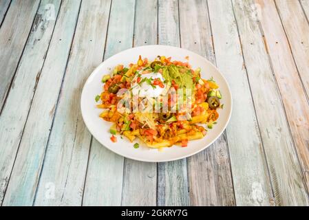 Pommes frites mit typischen Gewürzen eines Tellers mexikanischer Nachos mit Guacamole, Cheddar-Käse, Avocado, Tomaten, Petersilie und Jalapenos Stockfoto