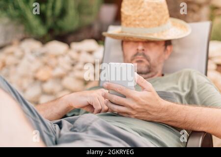 Freiberuflicher und digitaler Nomade, der morgens während des Sommerurlaubs auf der Apartmentterrasse am Smartphone arbeitet Stockfoto