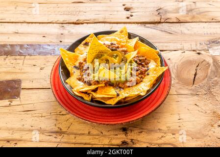 Mexikanische Nachos mit Guacamole, Jalapeno und Chili con Carne in schwarzer Schüssel Stockfoto