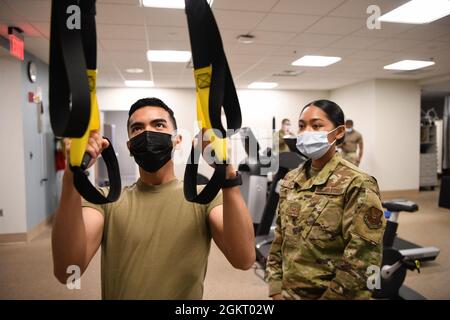 Leitender Airman May Cortez, Physiotherapeut, unterstützt Airman 1st Class Kyle Maglalang, Medizintechniker, während er eine Reihe mit dem Trainingsgerät für Ganzkörperwiderstand durchführt, 24. Juni 2021, in der Medizinischen Klinik bei F.E. Warren Air Force Base, Wyoming. Der TRX wird zur Stärkung und Stabilität des Oberkörpers eingesetzt. Stockfoto