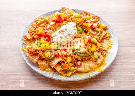 Mais-Nachos mit Frischkäse, Schweinefleisch, in Scheiben geschnittenen Gelee-Bohnen, dreifarbigen Paprika und Gratin Cheddar-Käse Stockfoto