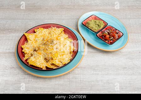 Mais Nachos au Gratin mit geriebenem Käse und Bohnen und zwei separaten Schüsseln Guacamole und Pico de gallo Stockfoto