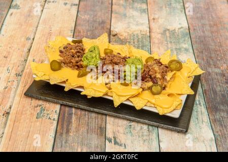 Chili con Carne Mais Nachos, Anklänge von Guacamole, geschmolzener Cheddar-Käse, Jalapeno-Brocken auf weißem Tablett Stockfoto