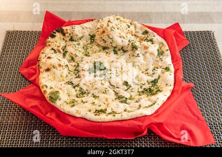 Traditionelles indisches Knoblauch-Naan, hergestellt in einem pakistanischen Restaurant in europa mit Mucho Petersilie und Sesamsamen auf grauem Untersetzer Stockfoto