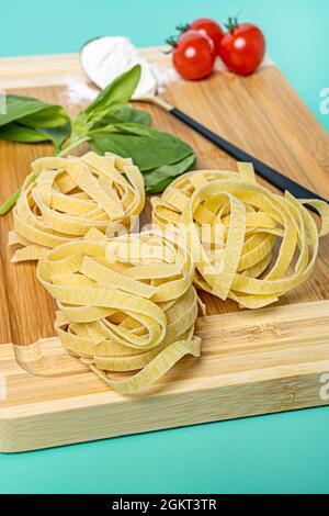 Frische Nudelnester mit Basilikum- und Kirschtomaten zur Zubereitung eines italienischen Pasta-Rezepts Stockfoto