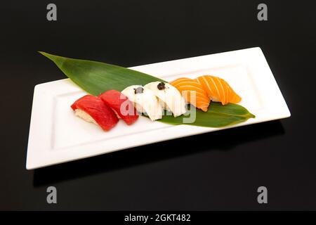 Bandeja de nigiri clásico de tres sabores, pez mantequilla trufado, salmón marinado y atún rojo en hoja de plátano Stockfoto