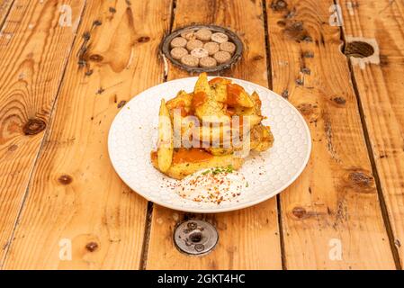 Spanische Tapa mit Patatas Bravas mit separaten Saucen auf schönem weißen Teller und einem Kiefernholztisch Stockfoto