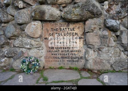 Nahaufnahme der Inschrift auf dem Culloden-Denkmal, die an die Schlacht hier zwischen den schottischen Jakobiten und den Engländern erinnert. Blumenkranz zur Seite. Stockfoto