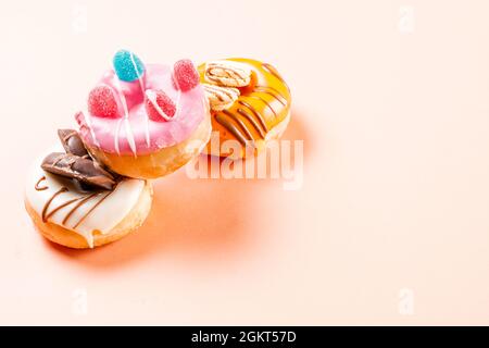 Foto von 3 Donuts mit Jelly Beans verziert und mit Schokolade gezeichnet.das Foto ist im horizontalen Format auf einem cremefarbenen Hintergrund aufgenommen.die p Stockfoto