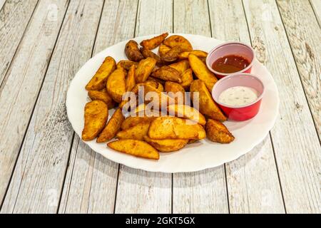 Portion Kartoffelkeile in Olivenöl mit Tomatensauce und Mayonnaise mit feinen Kräutern zum Eintauchen gebraten Stockfoto