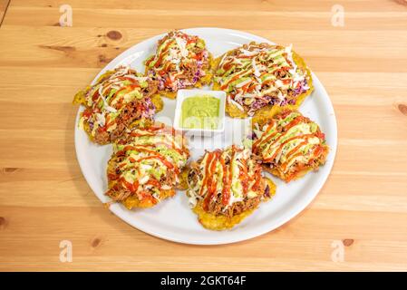 Teller mit typisch venezolanischem Macho-Kochbananen-Patacon mit zerfetztem Fleisch, Tomatensauce, Mayonnaise und Avocado auf Holztisch Stockfoto