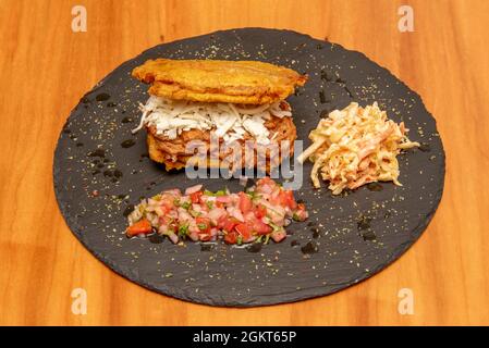 Großer Kochbananen-Patacon, gefüllt mit Käse und zerfetztem Fleisch mit cole Slaw und Pico de gallo auf einem schwarzen Schieferteller Stockfoto