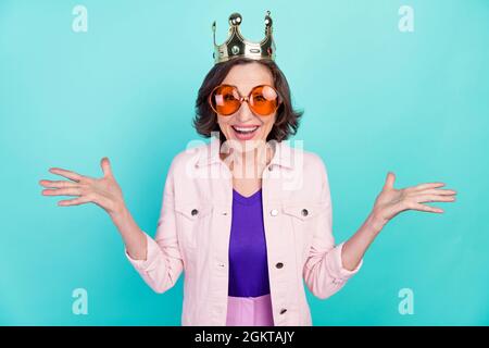 Foto Porträt Frau trägt goldene Krone Sonnenglas lächelnd überrascht isoliert lebendige türkise Farbe Hintergrund überrascht Stockfoto