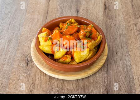 Spektakuläre Portion Patatas bravas a la madrileña in einem Tontopf auf einem Holztisch Stockfoto