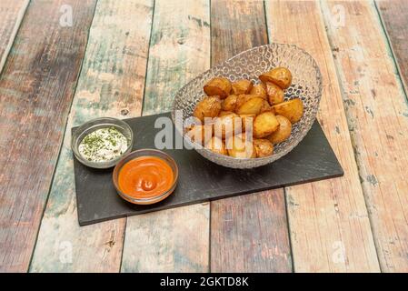 Aktualisierte Version von gebratenen Patatas Bravas mit der Haut und begleitet von würziger Sauce und Mayonnaise auf Holztisch Stockfoto