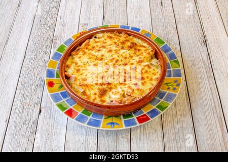 Portion gebratene Kartoffelkeile mit Speck und viel Käse-Gratin in einem Tontopf gebacken Stockfoto