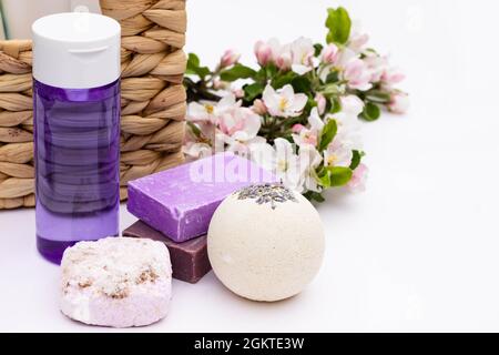 Flieder Kosmetikflasche, Badebombe, handgemachte Seife, Badesalz in der Nähe von Korbkorb mit Birnenblüten auf weißem Hintergrund. Natürliche Bio-Kosmetik conce Stockfoto