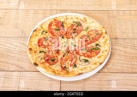 Kleine Pizza in Scheiben mit würzigen Pepperoni, Mozzarella-Käse und zerkleinerten Käse mit gehackter Petersilie, roter Zwiebel und gehacktem Basilikum auf einem Holztisch Stockfoto