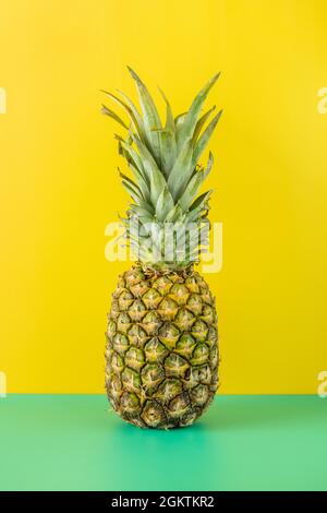 Reife Ananas auf schlichtem grünen Tisch und hellgelbem Hintergrund. Stockfoto