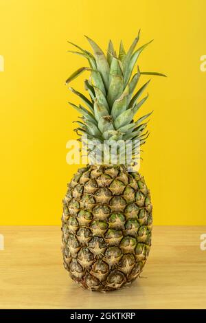 Ganze reife Ananas aus lateinamerika auf Kiefernholztisch und gelbem Hintergrund Stockfoto