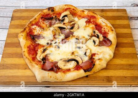 Pizza für eine Person mit viel geschmolzenem Mozzarella-Käse, in Scheiben geschnittenen Pilzen und geräuchertem Speck auf Bambusbrett Stockfoto