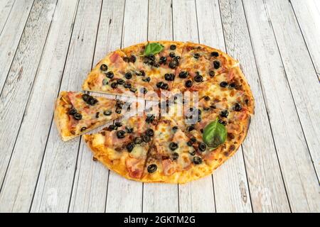 Sehr dünne Pizzascheiben mit Speck, Mozzarella-Käse, schwarzen Oliven in Scheiben geschnitten, Basilikumblättern und Tomaten Stockfoto