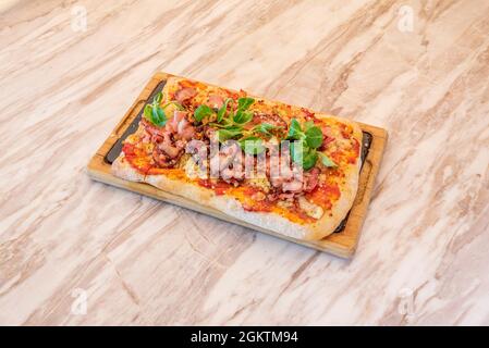 Rechteckige Pizza mit Carbonara-Rezept mit Lammsalat und viel gebratenem Speck, Tomaten und Mozzarella Stockfoto