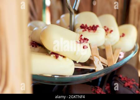 Cake Pops in weißer Schokolade in Form eines Mini-Eis auf einem Stock. Cake Pops werden mit trockenen Erdbeerbröseln garniert. Selektiver Fokus. Stockfoto